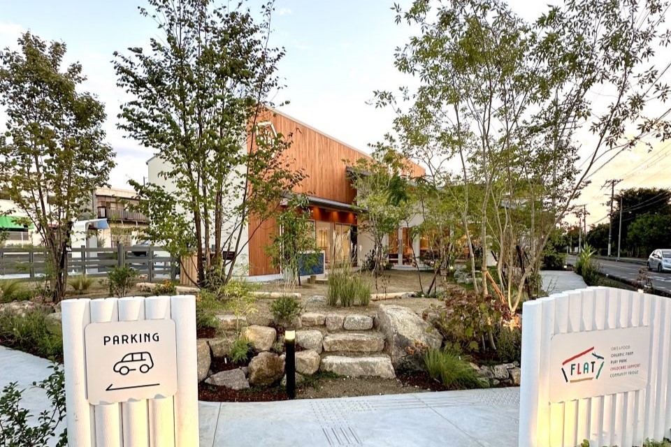 植木に囲まれた茶色の建物が特徴的な店の外観写真