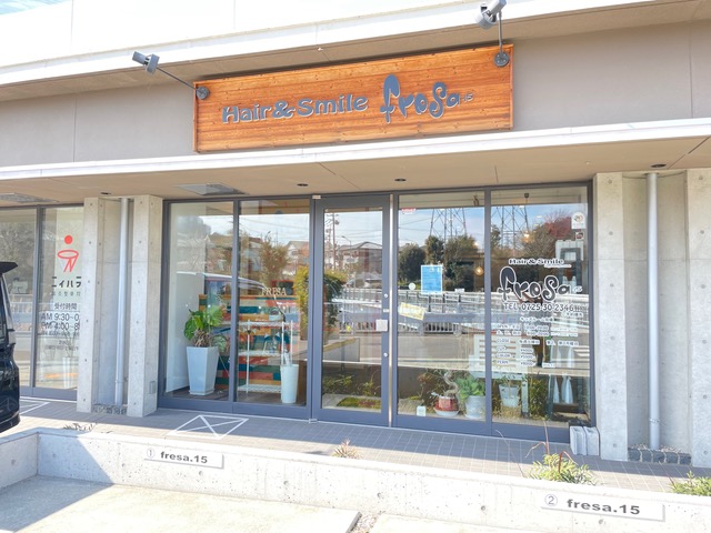 木製の看板に白い建物、ガラスの壁で店内が良く見える外観写真
