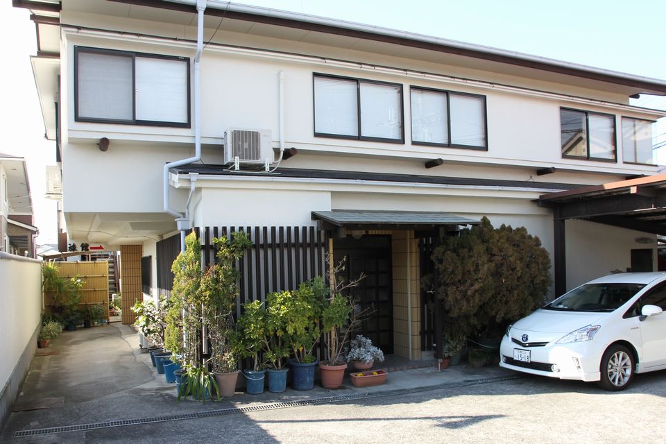 2階建ての白い建物、入り口には白い車がとめてある写真