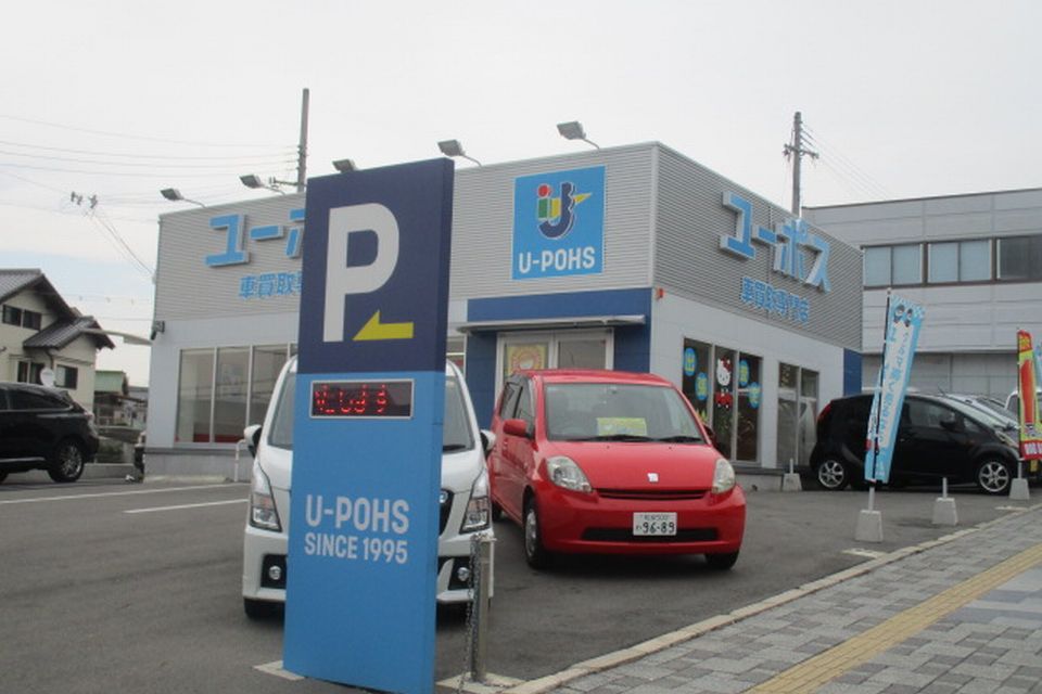 水色文字で「ユーポス」と書かれた灰色の建物と赤や白の車の写真