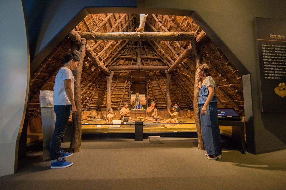 弥生時代の生活の様子を模した展示を眺める男女の写真