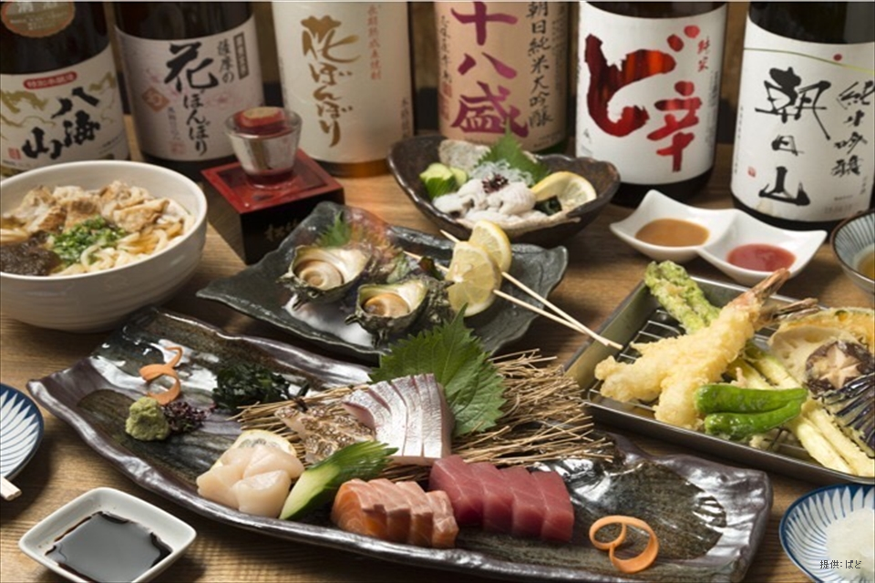 日本酒の瓶で囲まれた刺身やてんぷらなどの料理の写真