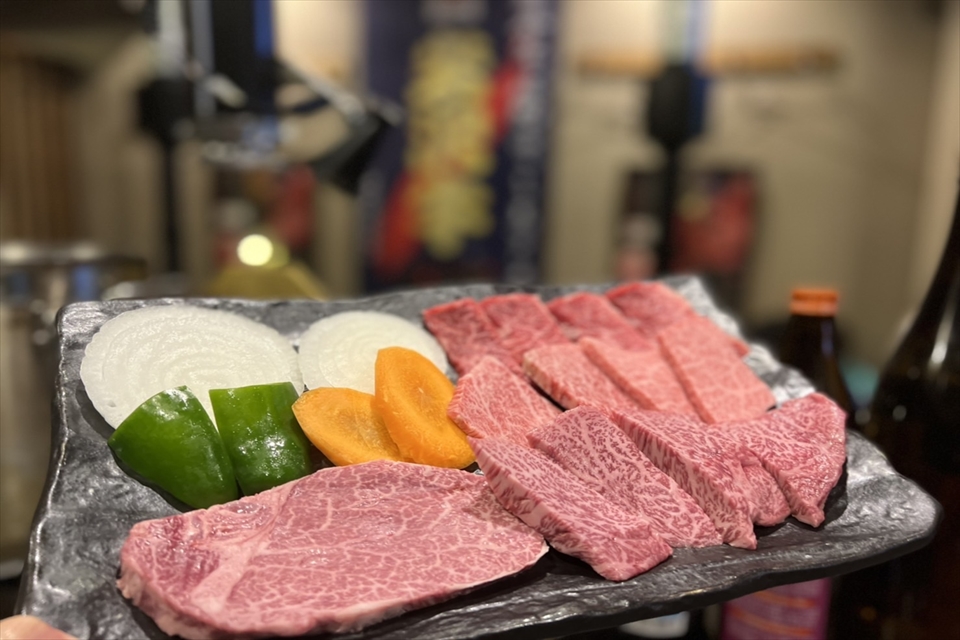 霜降り肉と玉ねぎなどの野菜が乗ったプレートの写真